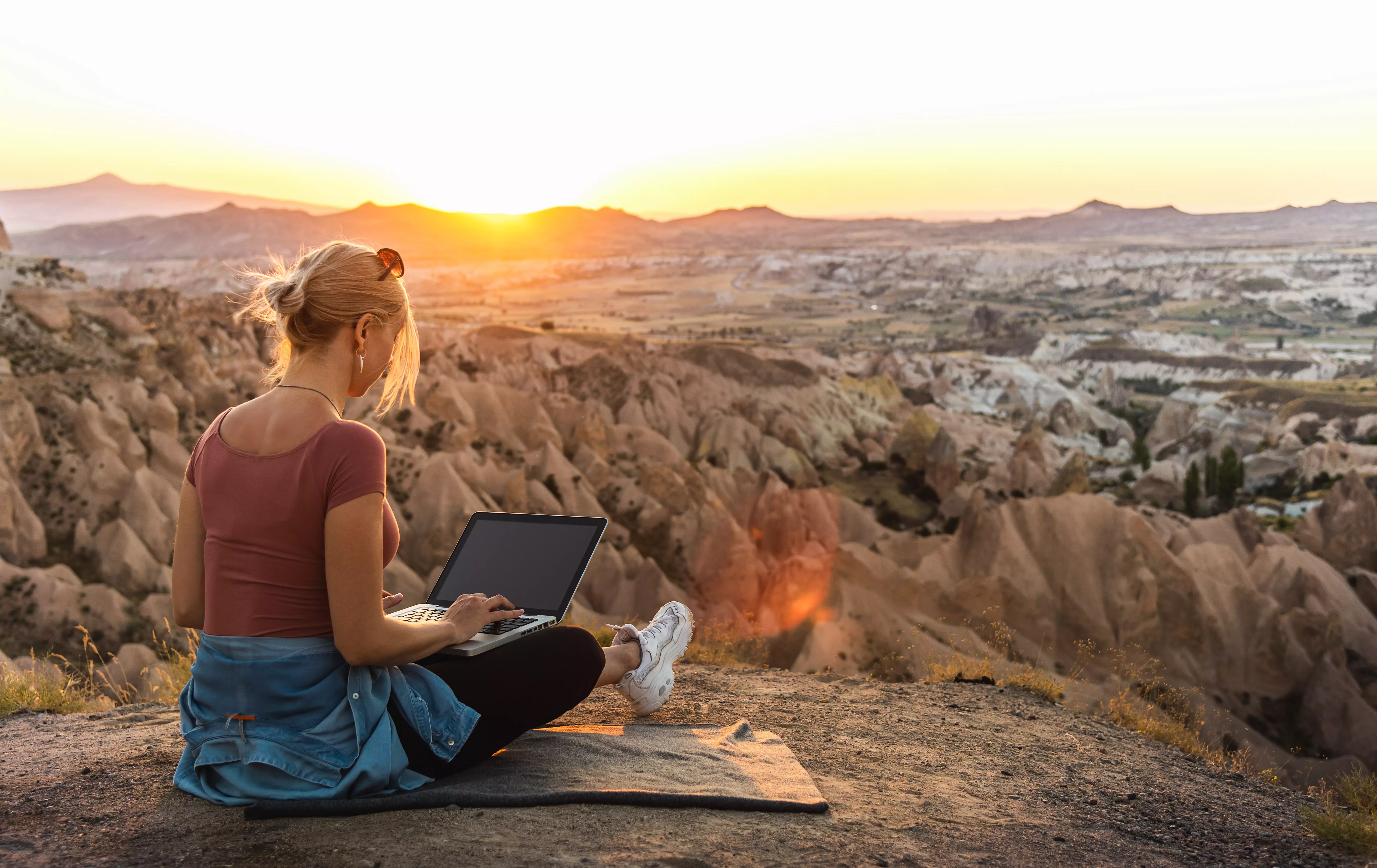 Young girl working at laptop at sunset on top of mountain Young girl working on laptop at sunset on top of mountain